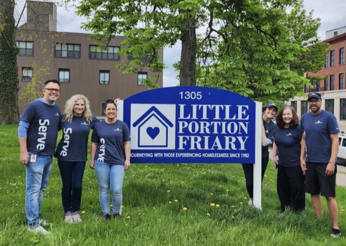workers and volunteers posed in front of a sign that reads "Little Portion Friary"